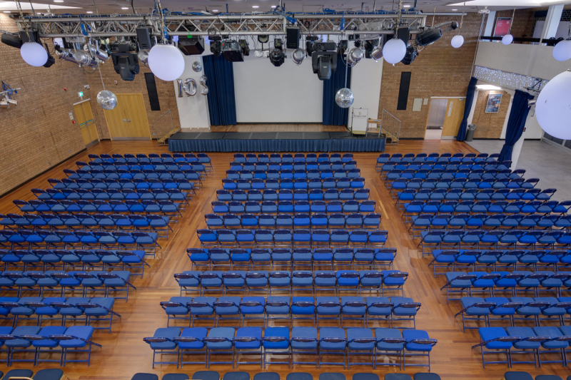 Large Hall, with a stage and many rows of chairs, all setup for a presentation event