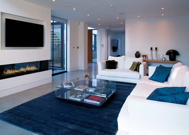 Large fireplace, with large TV over in a recess, with two and three piece white leather seating along with a large glass coffee table