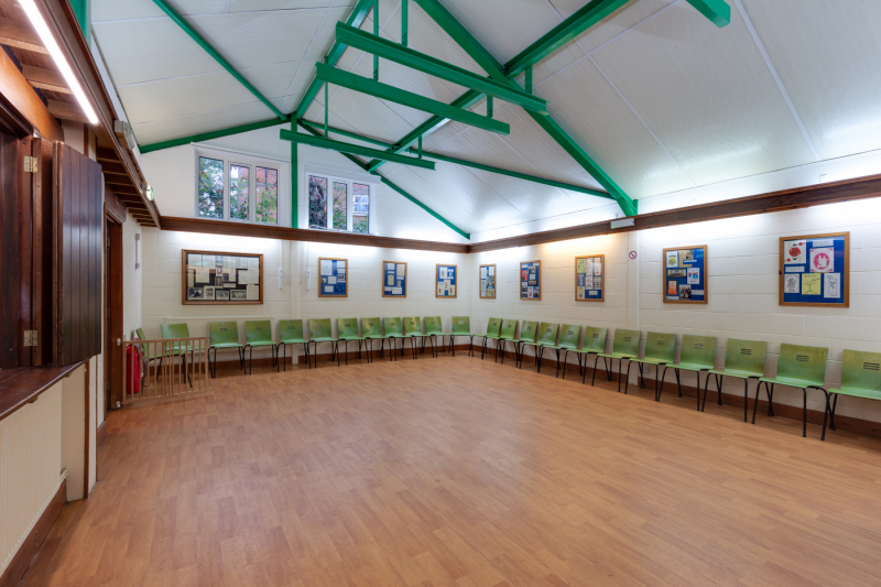 Gainsford Room at Woodside Hall, with kitchen serving hatch on one side and chairs along two edges of the walls.