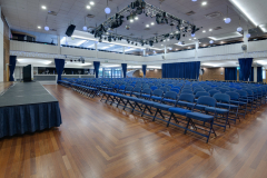 Large Hall, with a stage and many rows of chairs, all setup for a presentation event